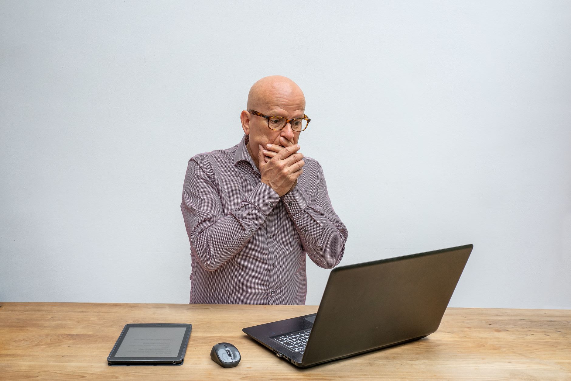 a senior man looks at a laptop screen with a worried expression
